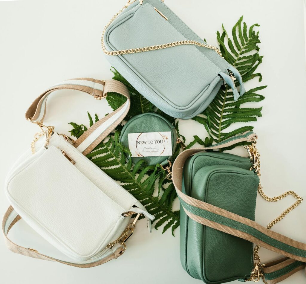 Flatlay of stylish leather handbags on a backdrop of green fern leaves. Perfect for fashion lovers.